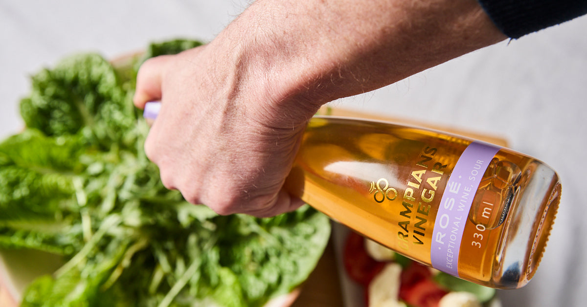 Hand holding a bottle of Grampians Vinegar next to leafy greens
